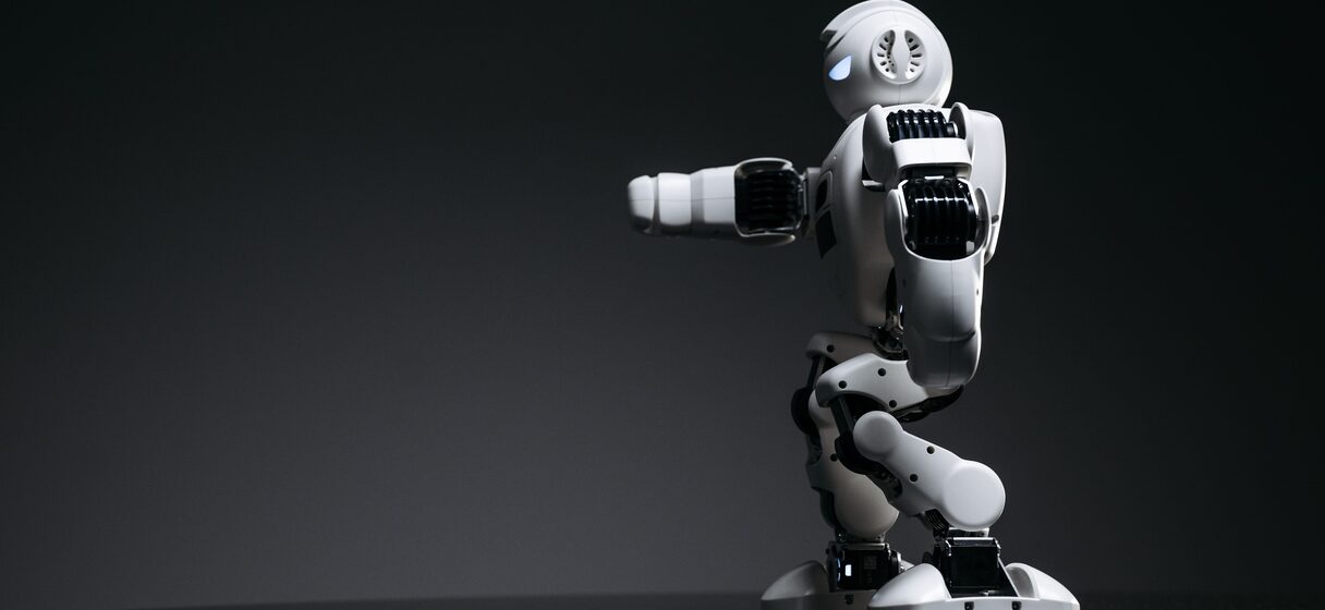A humanoid robot mid-stride in a darkened lab, lit from the side